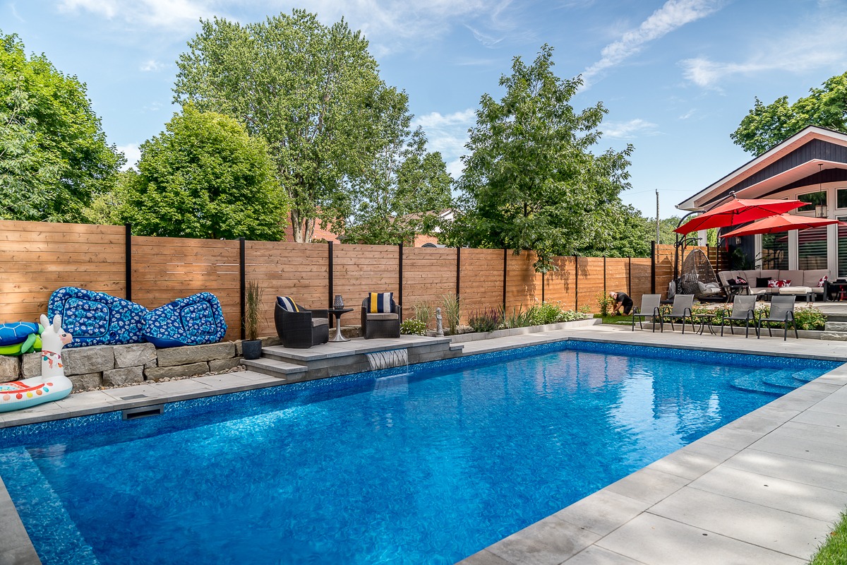 Backyard pool with wooden fence and patio furniture.