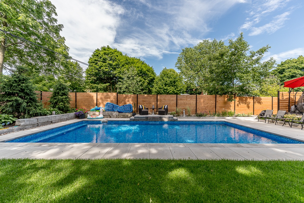 Backyard pool with lounge chairs and lush greenery.