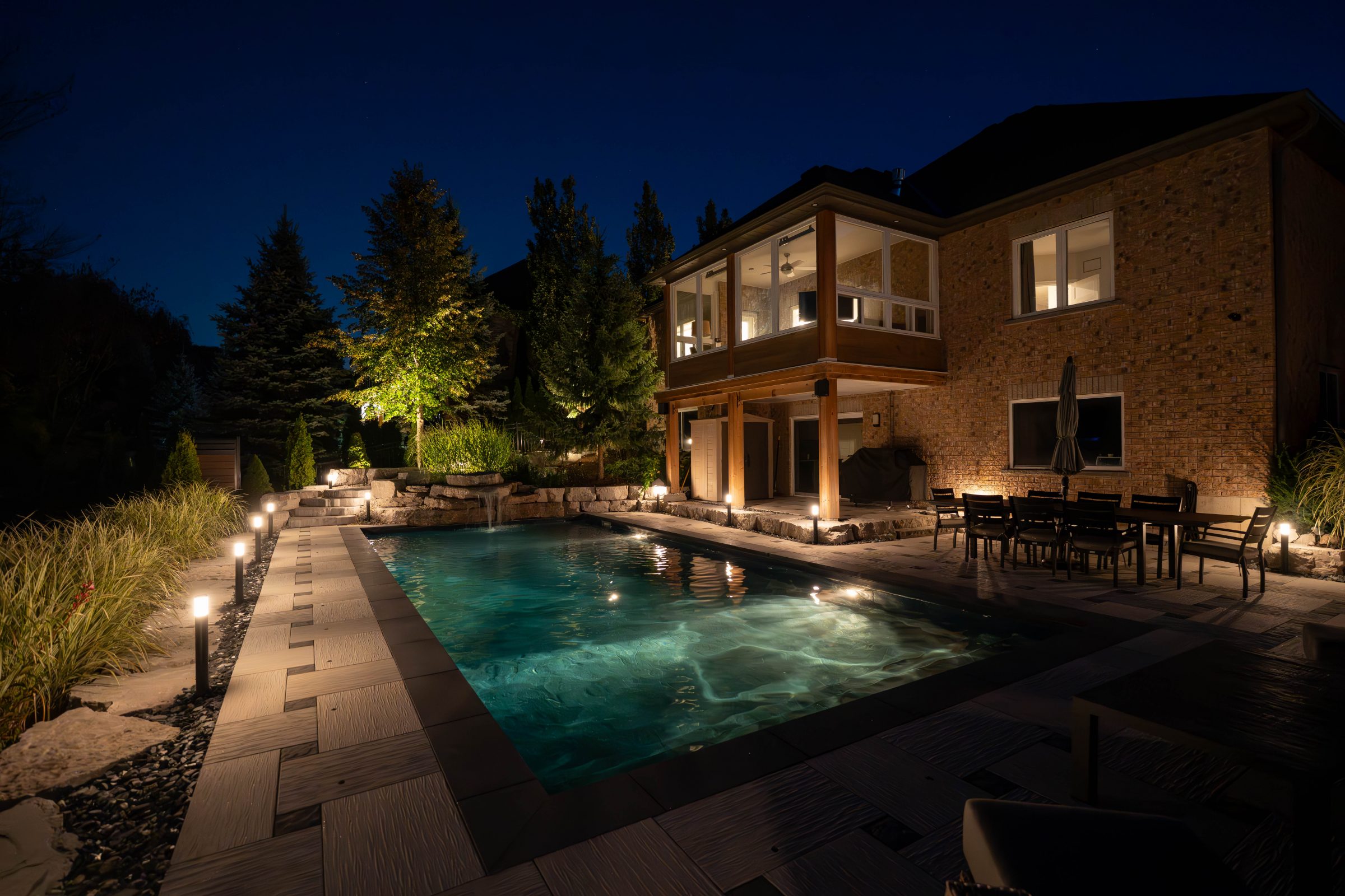 Illuminated backyard pool at night with lights on.