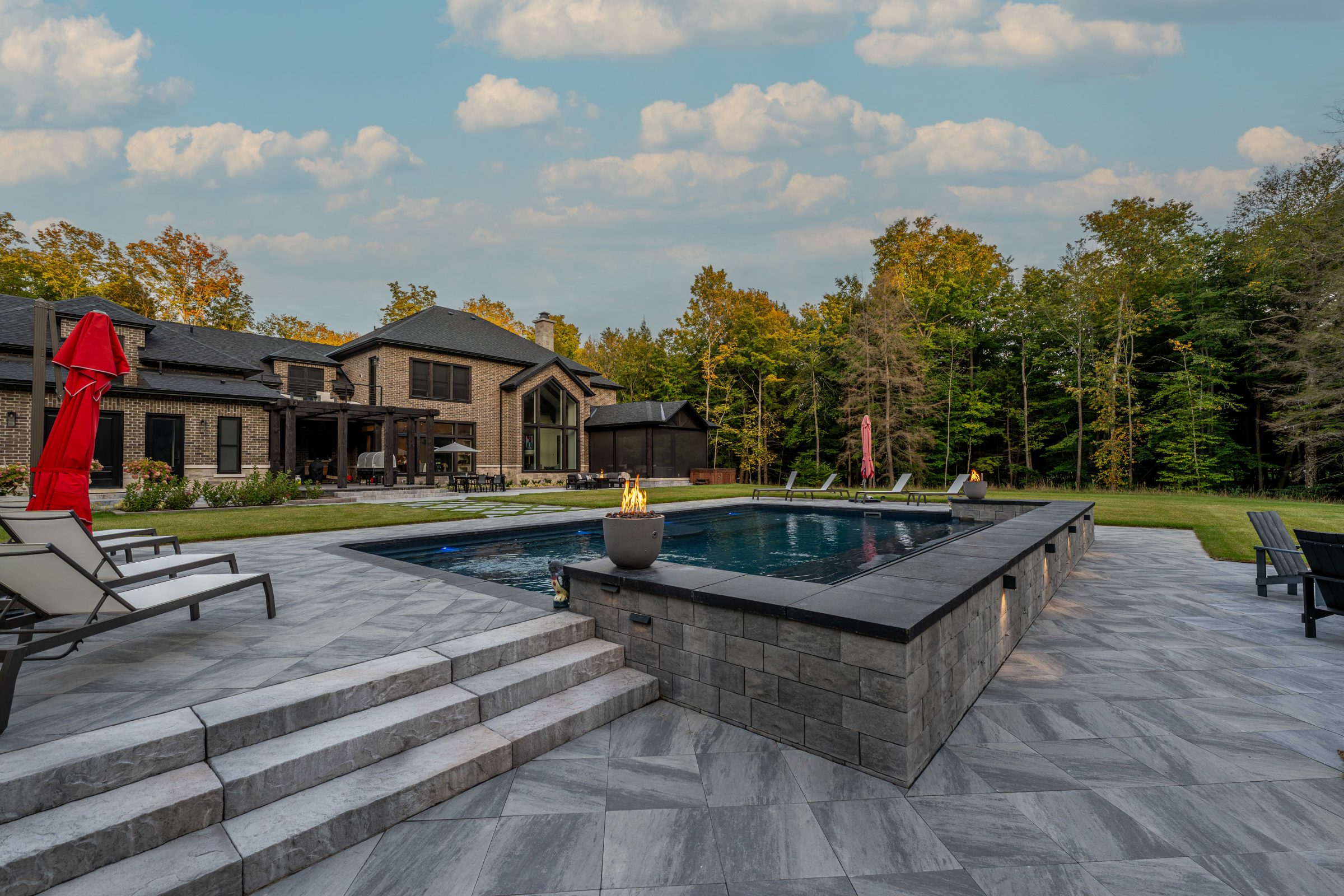 Luxurious home with pool and patio, surrounded by trees.