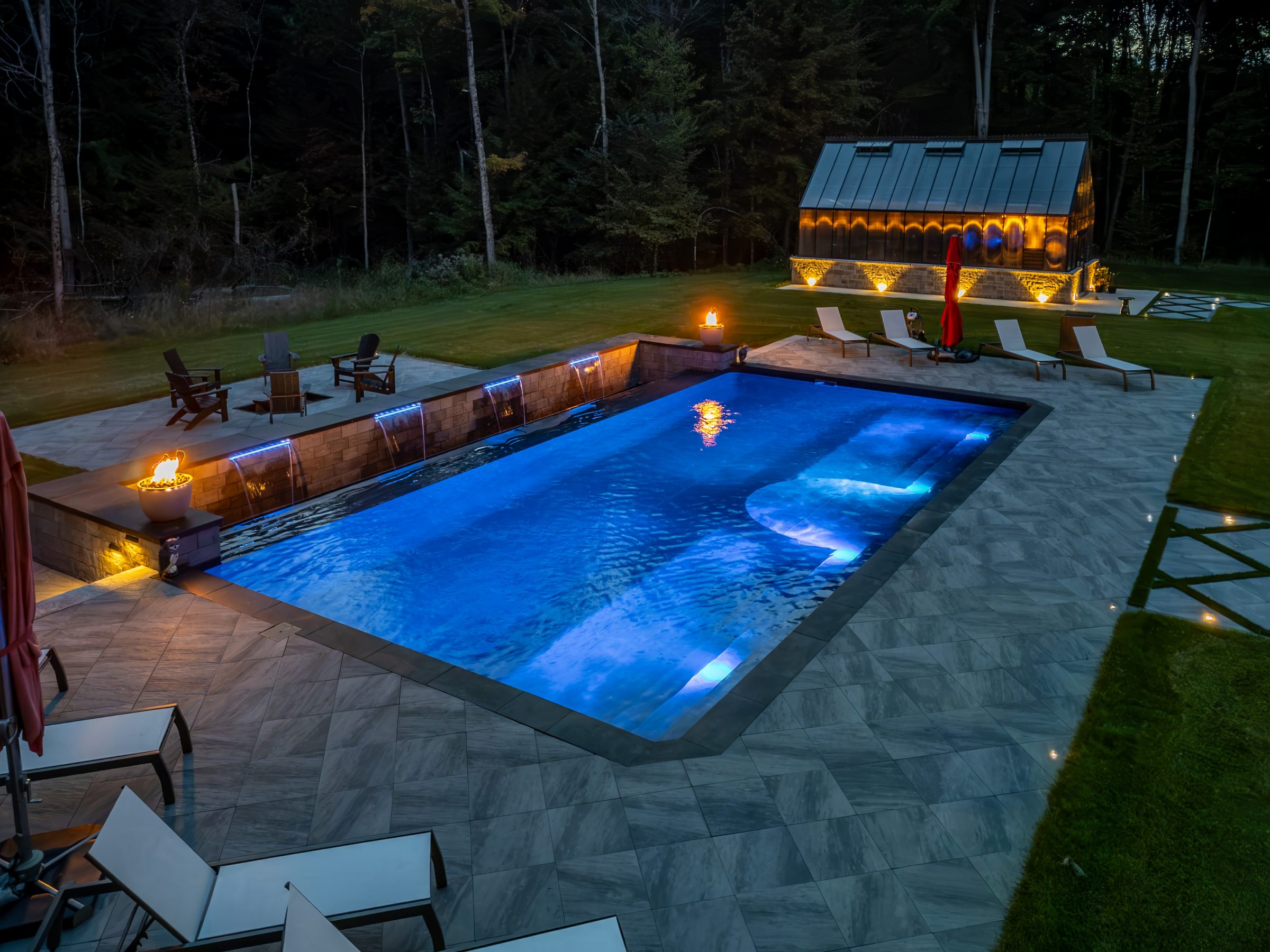 Luxurious backyard pool with lounge chairs at night.