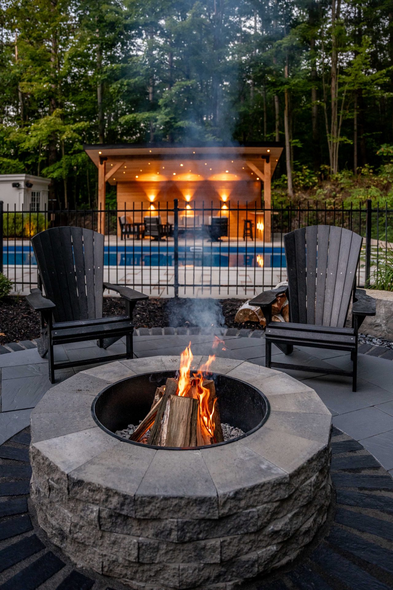 Backyard fire pit with chairs and lit gazebo.