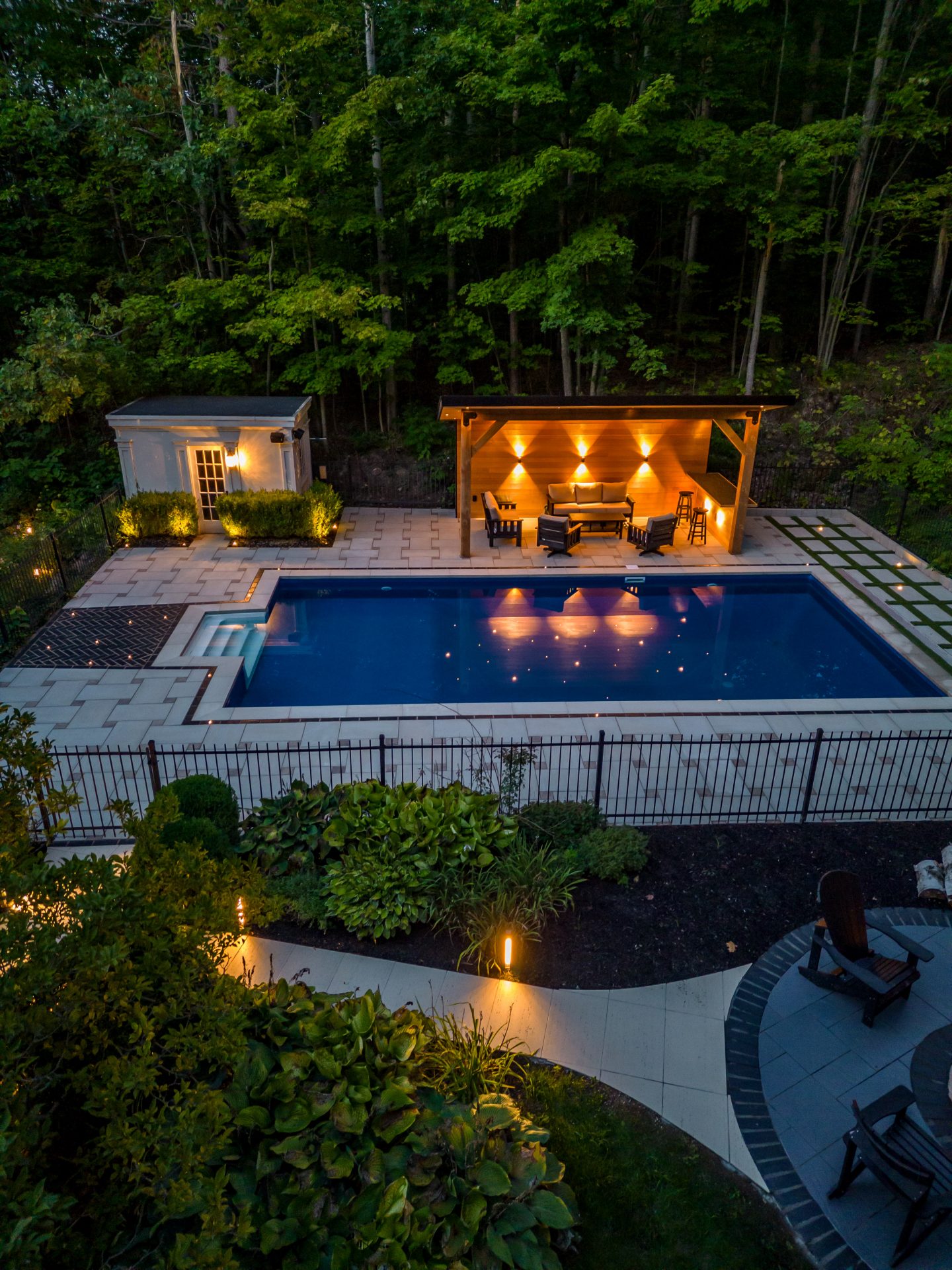 Illuminated backyard with pool and seating area.