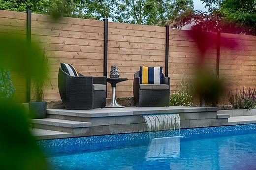 Cozy patio chairs by a pool and wooden fence.