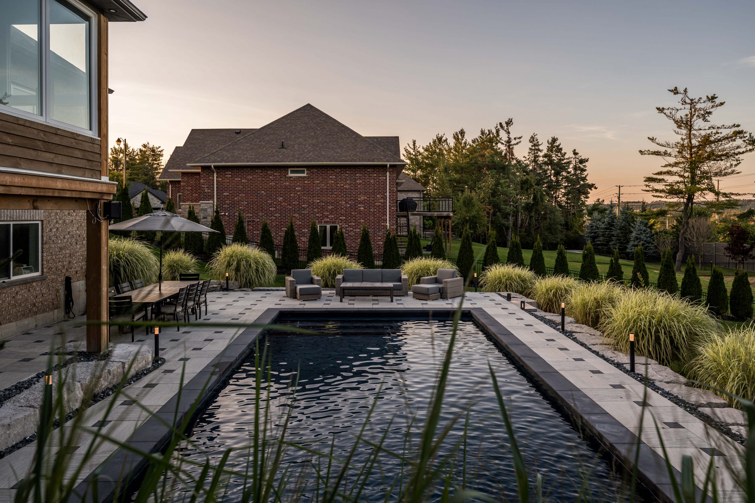 Backyard pool with seating and patio at sunset.