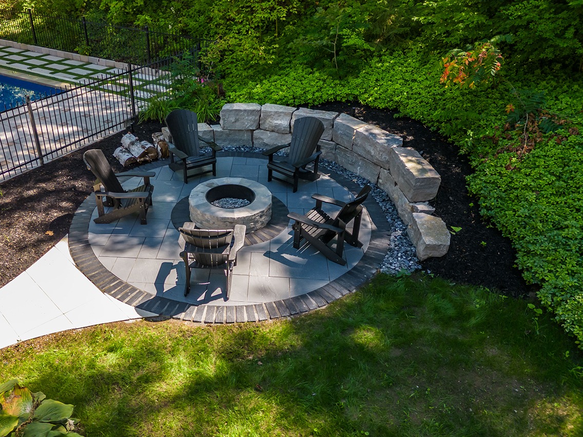 Backyard fire pit area with chairs and greenery.