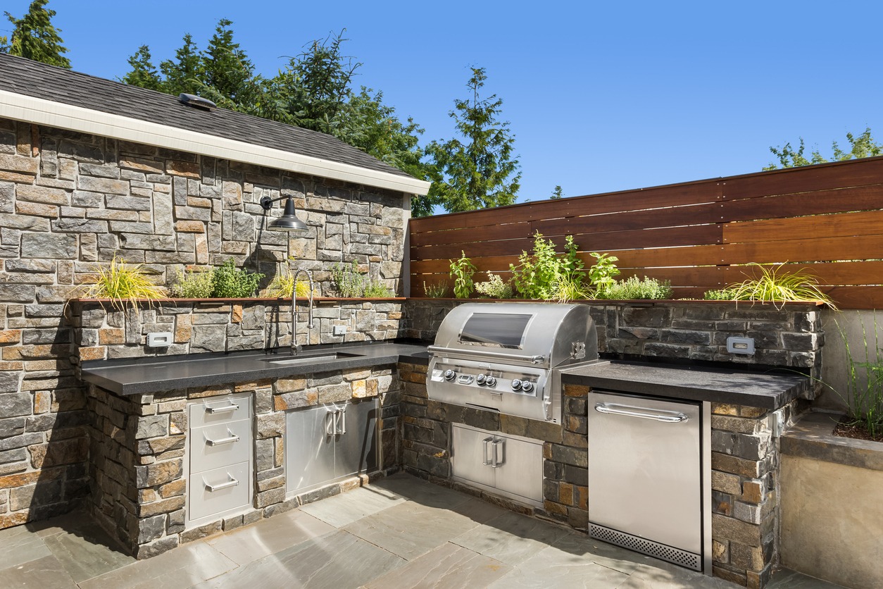 Outdoor stone kitchen with grill and herb garden.
