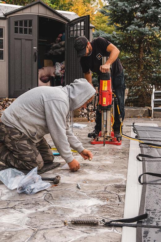 Two workers installing stone patio outdoors.