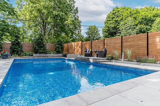 Backyard pool with wooden fence and lounge chairs.